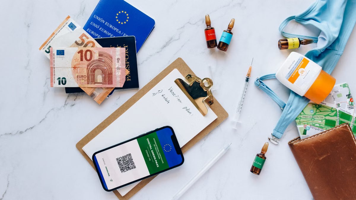 Flat lay of travel essentials including vaccination passport, euros, and medical supplies.